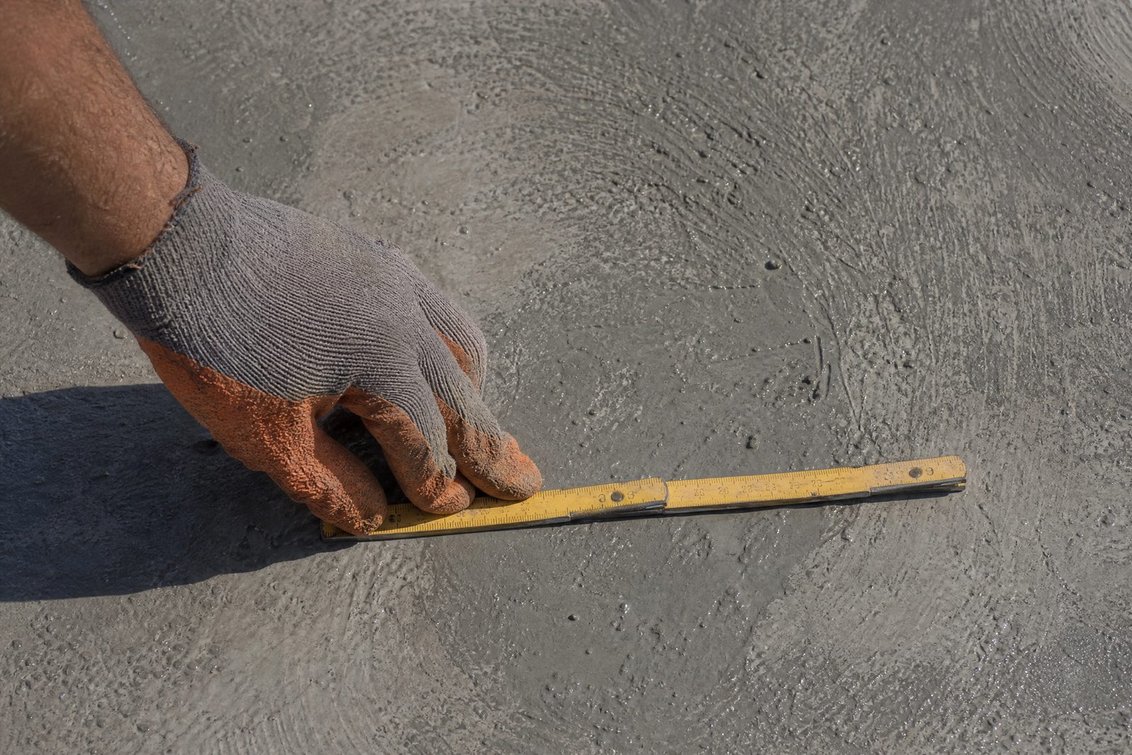 Main gantée posant un mètre pliant à plat sur une dalle de béton fraîchement talochée.